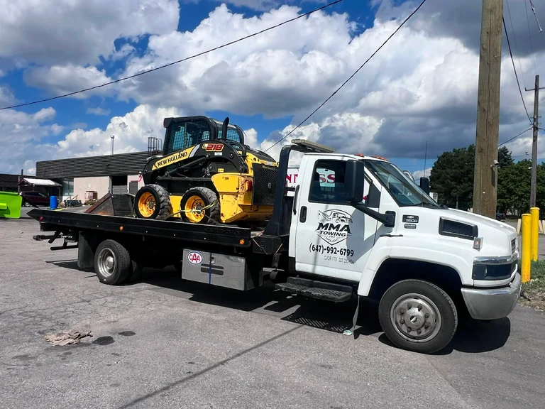 MMA Towing flatbed hauling a New Holland skid steer loader in the GTA