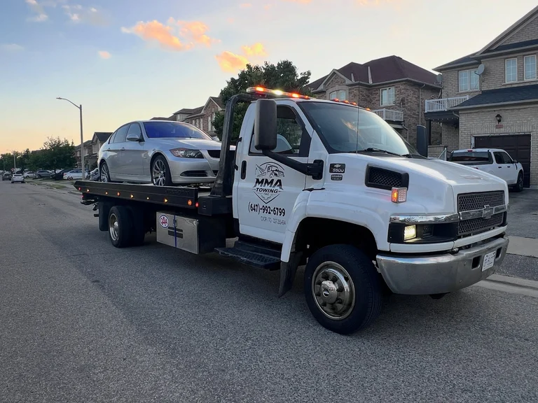 MMA Towing flatbed carrying a sedan in a GTA neighbourhood at sunset